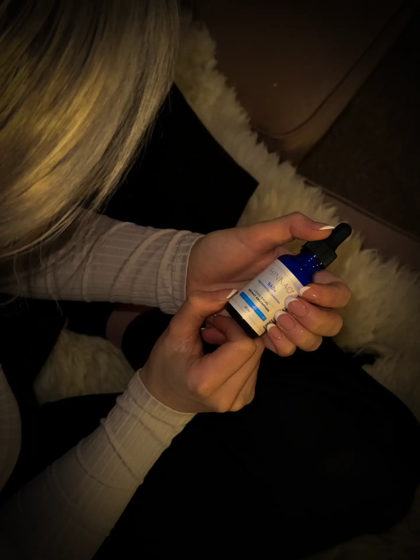 Woman holding a HINNAO NAD+ sublingual dropper bottle at home
